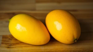 Close-up of ripe and unripe mangoes side by side on a wooden surface, showing color progression from green to golden yellow-orange, natural daylight, realistic fruit detail