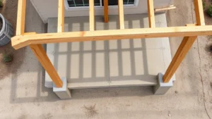 Overhead view of residential patio cover frame with pressure-treated wood posts and aluminum beam connections during construction, showing concrete footings and proper post spacing on sandy Florida soil