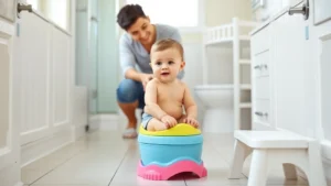 Child sitting on colorful child-sized potty seat in bright, welcoming bathroom with step stool nearby, parent supervising supportively in background