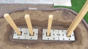 Overhead view of concrete post footings set in ground with pressure-treated wooden posts installed vertically, showing proper spacing and plumb installation on a residential backyard construction site