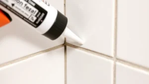 Close-up of fresh white caulk bead being applied into a bathroom tile corner with a caulking gun, showing smooth professional application technique and wet caulk surface