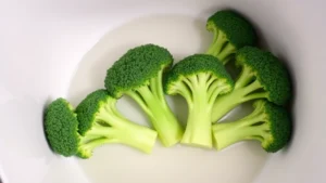 Fresh raw broccoli florets arranged in a white microwave-safe bowl with water at the bottom, ready for steaming, overhead view, bright kitchen lighting, clean modern aesthetic