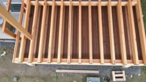 Overhead view of pressure-treated deck framing with installed joists, beams, and rim boards, showing proper spacing and connections on residential house foundation