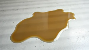 Close-up of fresh motor oil spill on light gray concrete garage floor with clear liquid pooling, photorealistic detail showing surface texture